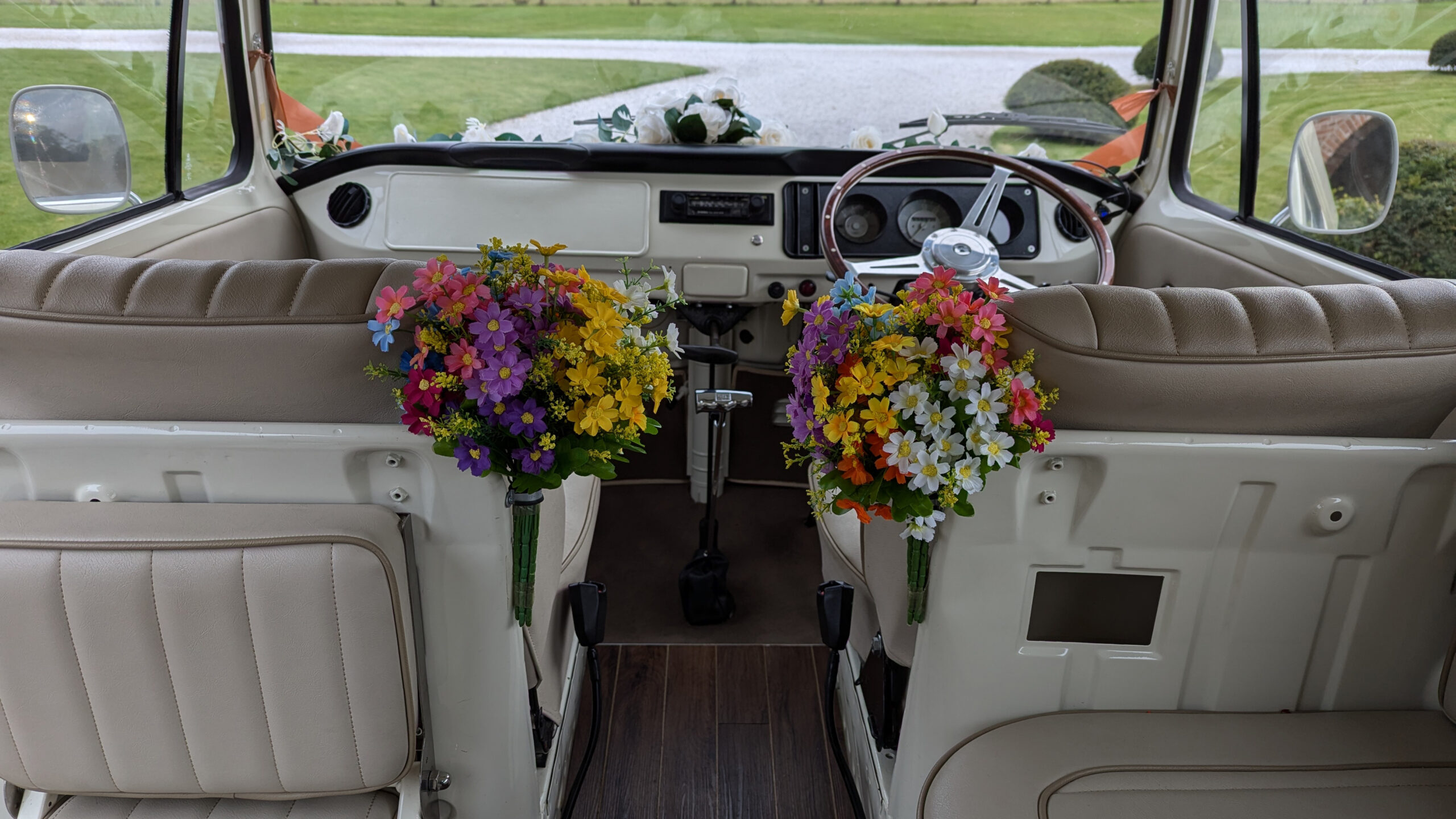 Interior of a vintage VW campervan decorated with wedding flowers, showing the front seats and classic dashboard.